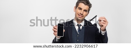 cheerful businessman in braces holding smartphone with blank screen and credit card isolated on grey, banner