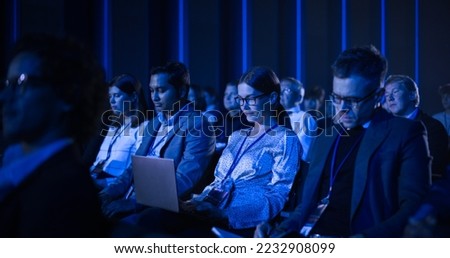 Female Sitting in a Dark Crowded Auditorium at a Tech Conference. Young Woman Using Laptop Computer. Specialist Watching Innovative Technology Presentation About New Software and High Tech Products. Royalty-Free Stock Photo #2232908099