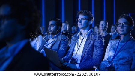 Male Sitting in a Dark Crowded Auditorium at a Tech Conference. Professional Using Laptop Computer. Specialist Watching Innovative Technology Presentation About New Hardware and High Tech Solutions. Royalty-Free Stock Photo #2232908107
