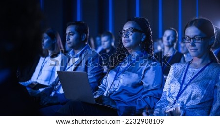 Black Female Sitting in Dark Crowded Auditorium at an International Business Conference. Multiethnic African Woman Using Laptop Computer. Delegate Watching Presentation About New Financial Solutions. Royalty-Free Stock Photo #2232908109