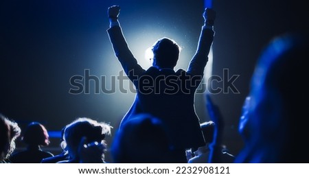 Young Excited Man Ecstatic About Winning the Coveted Business Person of the Year Award. Man Jumping After Winning the Event Category. Handsome Specialist Celebrating and Cheering a Colleague on Stage. Royalty-Free Stock Photo #2232908121