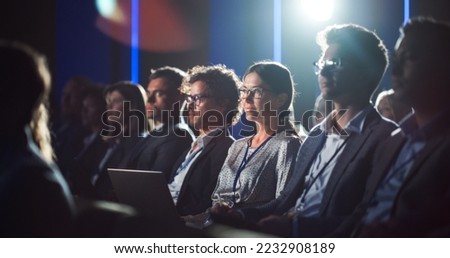 Crowd of Business People in Dark Conference Hall Watching an Innovative Inspiring Keynote Presentation. Business Technology Summit Auditorium Room Full of Corporate Delegates. Royalty-Free Stock Photo #2232908189