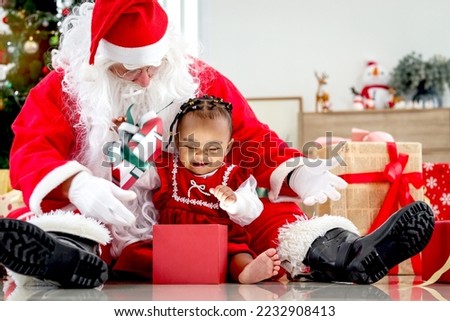 Adorable happy smiling African American child girl sitting on Santa Claus lap around decorative Christmas tree, kid open Christmas gift box present, feeling surprised and excited
