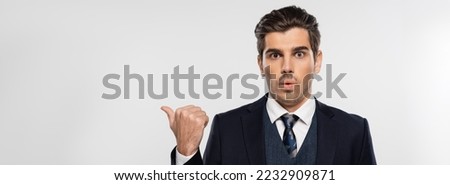stunned businessman in suit pointing with thumb away isolated on grey, banner