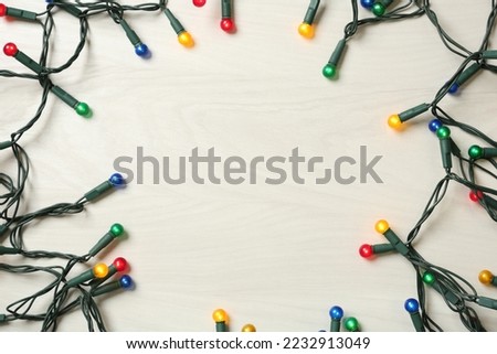 Frame of beautiful glowing Christmas lights on white wooden background, top view. Space for text