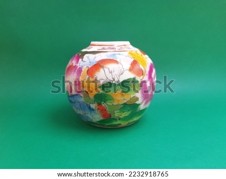 Small ceramic jars as indoor decoration with beautiful colorful ornaments on the outside, isolated on a green background