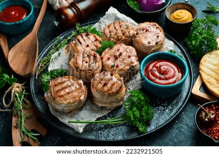 Grilled medallions wrapped in bacon. in a pan, ready to eat. On a black concrete background. Top view.