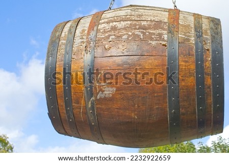 large wooden barrel suspended from a chain at a coopers barrel maker. Wooden barrel with a background of sky, varnished. 