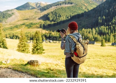 Photographer woman with yellow backpack is taking a picture of autumn landscape in mountains. Tatras, Poland