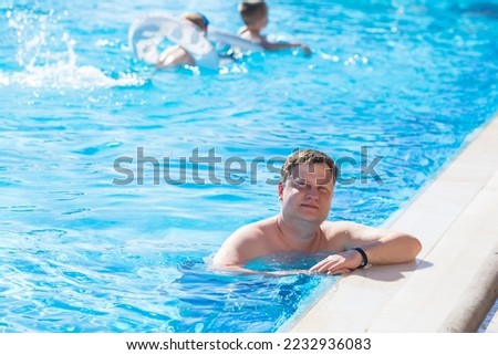 Young blond man swims in the pool with children.