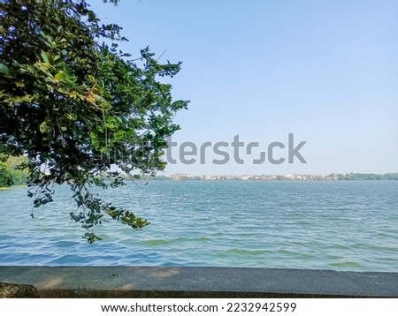 Stock photo of beautiful Rankala lake, old stone retaining wall around the lake, branches of the green tree overhanging on water . Picture captured under bright sunny light at kolhapur, Maharashtra.