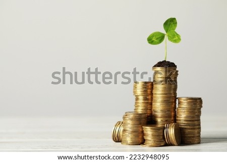 Stacked coins and green sprout on white wooden table, space for text. Investment concept