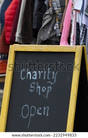 Handwritten sign for charity shop with clothes rail in the background