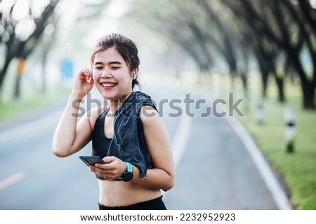 Portrait of sporty asian fitness woman listen to music from smartphone with bluetooth wireless headset in-ear, young asian girl hands holding mobile phone at workout at gym. Healthy wellness concept