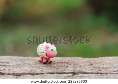Plasticine world - little homemade white sheep with green eyes stand on a wooden floor, selective focus and place for text 
