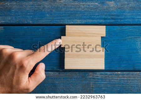 Conceptual image of business startup and stability - male finger pushing simple blank peg into a stack of them. Over textured blue wooden background.