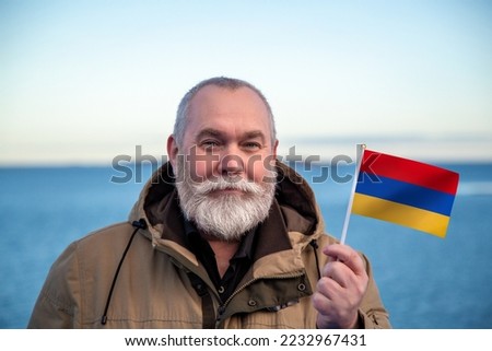 Man holding Armenia flag. 
Portrait of older man with a national Armenian flag. 
Visit Armenia concept. Older man 50 55 60 years old 
with gray beard outdoors travelling in winter. Travel to Armenia