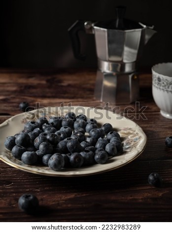 Breakfast plate of blueberries with coffee pot and mug on wooden table, dark food vertical picture