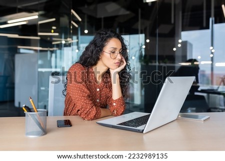 Sad grumpy Latin American woman working inside the office, business woman is bored looking at the laptop screen.