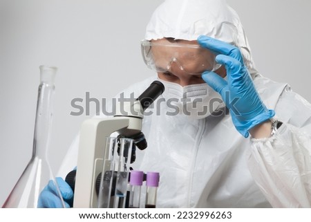 Scientific virologist. Biologist in protective suit and blue gloves using a microscope. Viruses concept. Virus University employee.