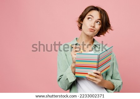 Young woman 20s she wear green shirt white t-shirt writing down in notebook diary remind memories and make list of dreams isolated on plain pastel light pink background studio People lifestyle concept