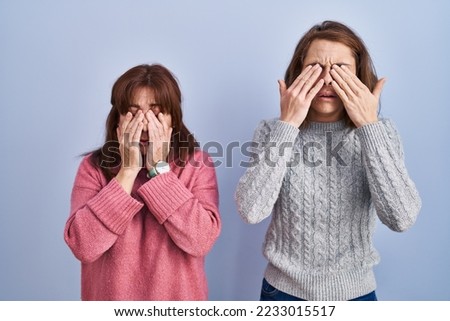 Mother and daughter standing over blue background rubbing eyes for fatigue and headache, sleepy and tired expression. vision problem 
