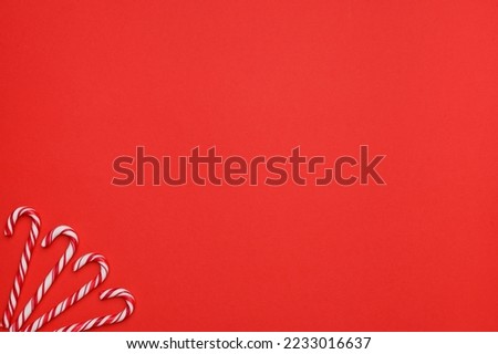 Layout of four white canes with red stripes, sweet Christmas candies on a red background. The concept of traditional Christmas sweets. Top view. Copy space.