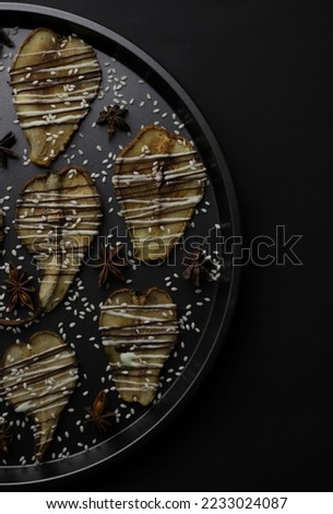 dried pears decorated with white and black chocolate and sesame seeds on a black tray and a dark background. for postcards menu labels calendars signs and stands