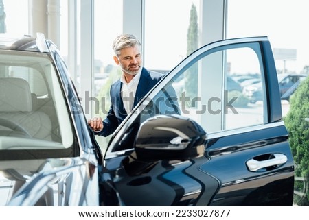 Mature handsome stylish man in car sales center. Mature man choosing new automobile. Royalty-Free Stock Photo #2233027877