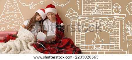 Little children in Santa hats reading book near beige wall with drawn living room