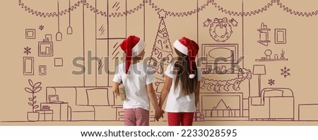 Little children in Santa hats and Christmas pajamas holding hands near wall with drawn living room