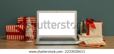 Laptop with Christmas presents and stationery on table near grey wall