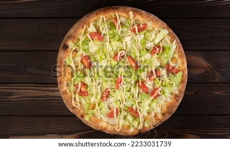 Pizza Caesar style with white sauce, chicken, parmesan, cherry tomatoes and fresh lettuce at wooden background, top view. Restaurant pizzeria menu concept