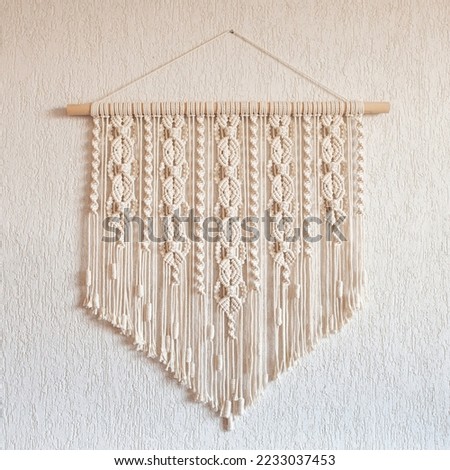 Handmade macrame wall decoration with wooden stick hanging on a white wall. Female hobby. ECO friendly modern knitting natural decoration in interior. Copy space Royalty-Free Stock Photo #2233037453