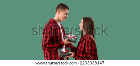 Happy young couple in checkered pajamas and with Christmas gifts on green background