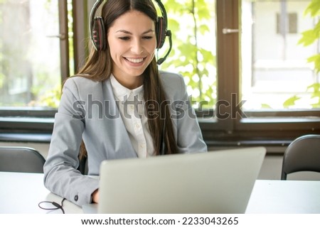 Young businesswoman with headset working on laptop in modern office. Royalty-Free Stock Photo #2233043265