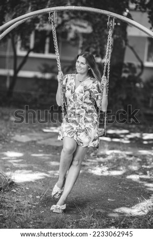 A woman with loose hair walks near her house and rides on a bright yellow swing