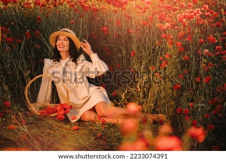 A girl in a white dress and with a basket of poppies is sitting on a poppy field.