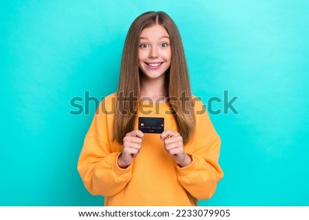 Photo of excited girl teenager wear trendy sweater hold plastic credit card want spend money entertainment weekend isolated on cyan color background