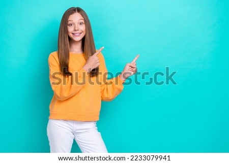 Photo of young cheerful teen girl wear orange pullover fingers direct empty space useful interesting information isolated on cyan color background