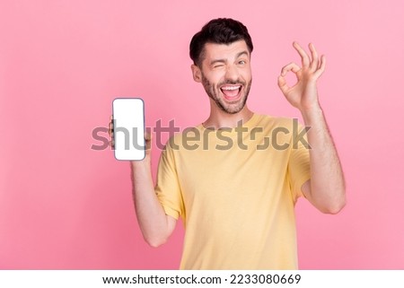Photo of funny guy winking eye hold modern gadget presenting new interface eshop ebank menu okey sign isolated on pink color background