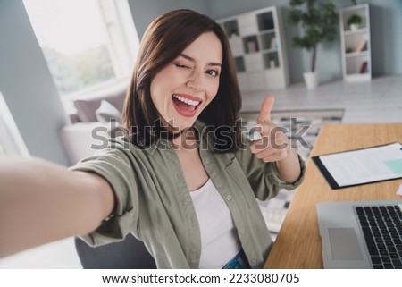 Portrait of positive pretty girl sit chair take selfie record video eye wink pointing finger you workplace indoors Royalty-Free Stock Photo #2233080705