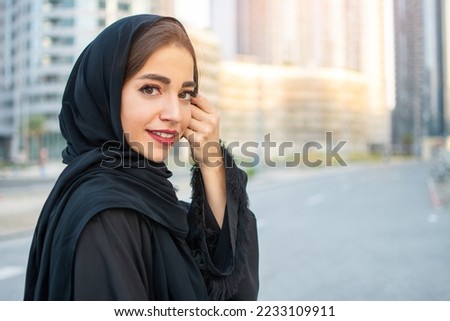 Portrait of beautiful Arabian young woman wearing traditional arabic clothing. Smiling Arabian woman holding veil with hand. Royalty-Free Stock Photo #2233109911
