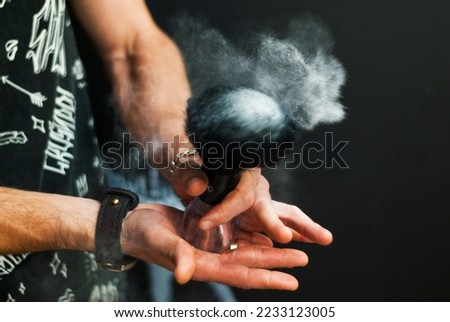 Men's hands hold a shaving brush from which talc scatters. Male stylist with shaving tools on a black background. Barber at work. Hair and beard care. Barbershop. Royalty-Free Stock Photo #2233123005