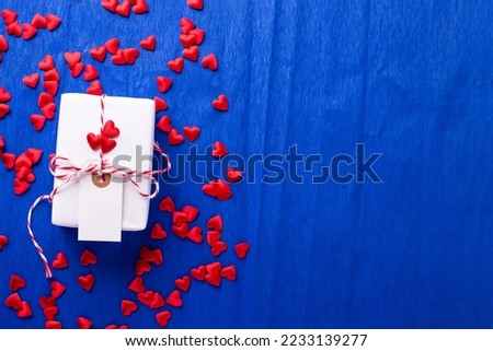 Wrapped box with present and empty tag and many red little hearts  on  electric blue textured  paper background.  Place for text. Top view. Romantic postcard.
