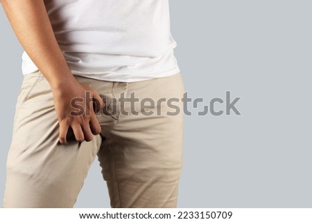 Asian man in reaction of scratching crotch on grey background, closeup. Annoying itch or Tinea Cruris. Human body problem or healthcare and medicine concept. Royalty-Free Stock Photo #2233150709