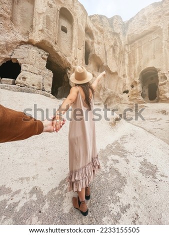 Happy young woman on background of ancient cave formations in Cappadocia following by the man. The Monastery is one of the largest religious buildings.