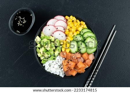 Poke bowl with salmon, rice, cucumber, corn, radish, avocado and sauce on a black background, top view. Balanced diet food. Hawaiian traditional food. High quality photo