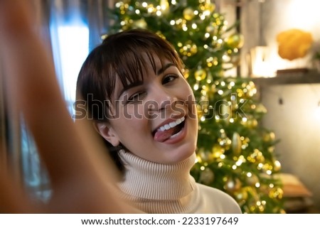 Close-up portrait of beautiful caucasian brunette woman in white sweater taking selfie photo standing by Christmas tree at night. Selective focus. People theme.	