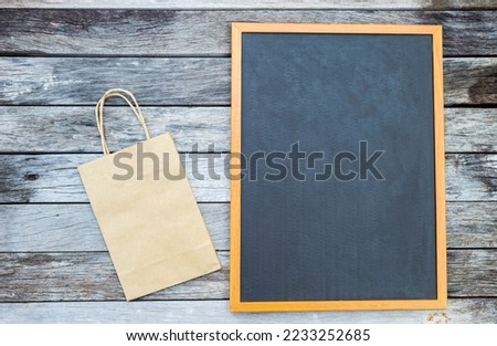 Black board with paper bag on wood background, blank promotion sign with paper shopping bag
